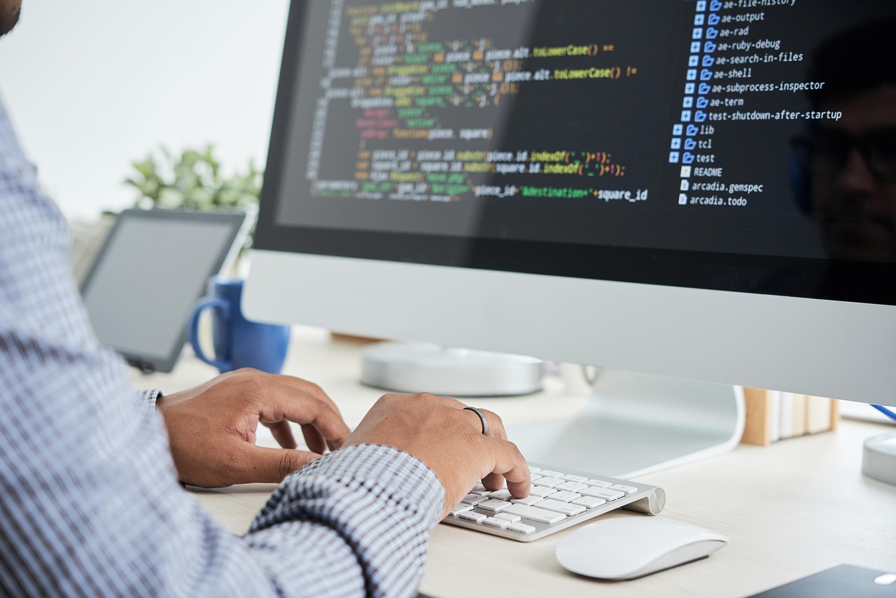 Mãos a escrever código num teclado, com um editor aberto no monitor.